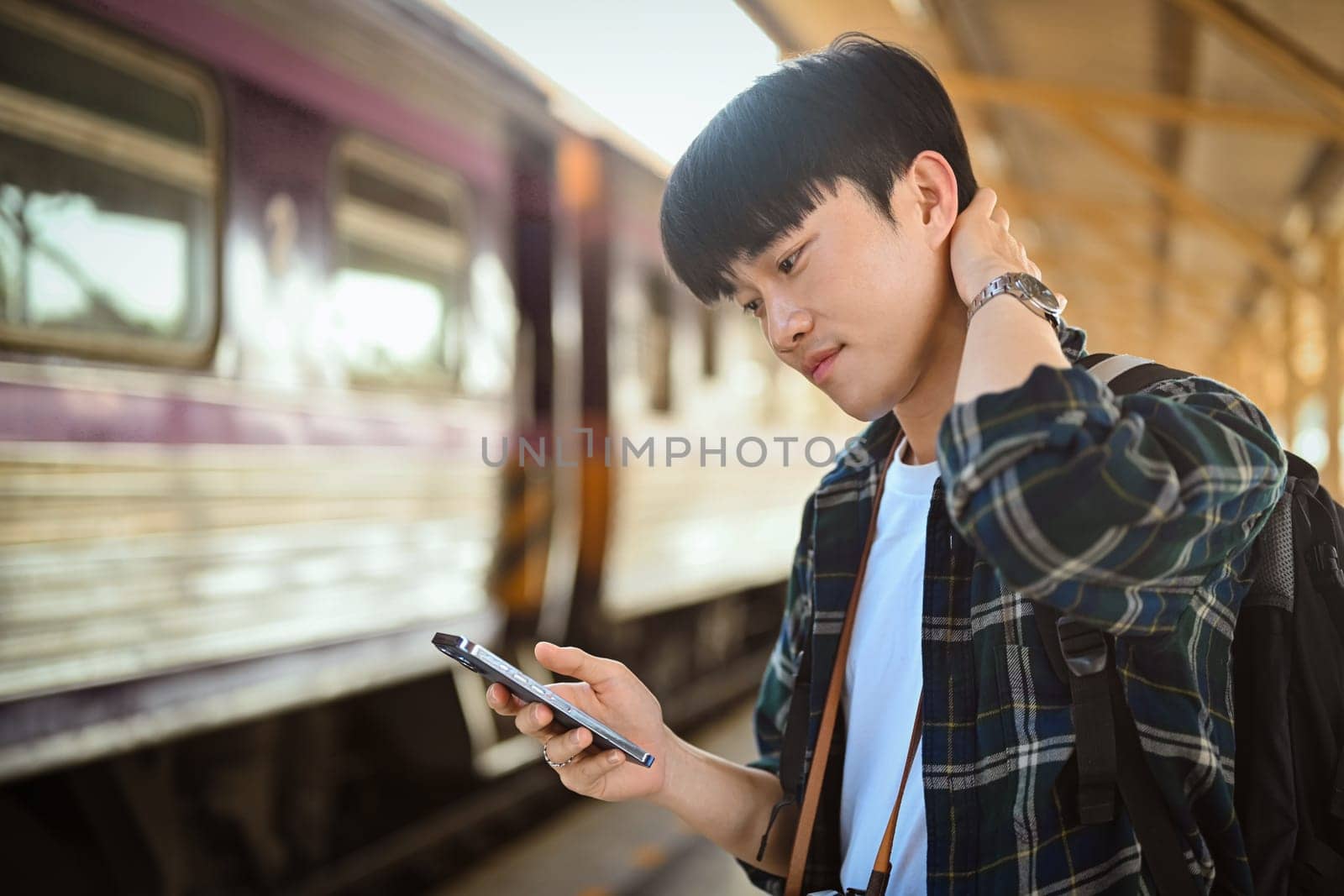 Handsome male traveler checking timetable train schedule for trip with application on smartphone by prathanchorruangsak