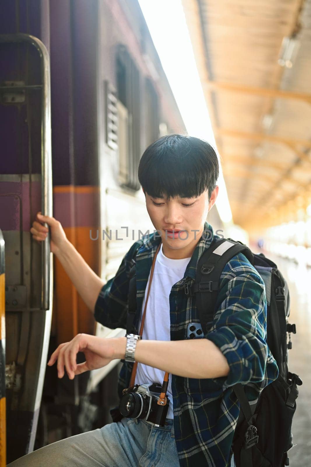 It's time to get on the train. Traveler male with backpack checking time on wrist watch and getting on the train by prathanchorruangsak