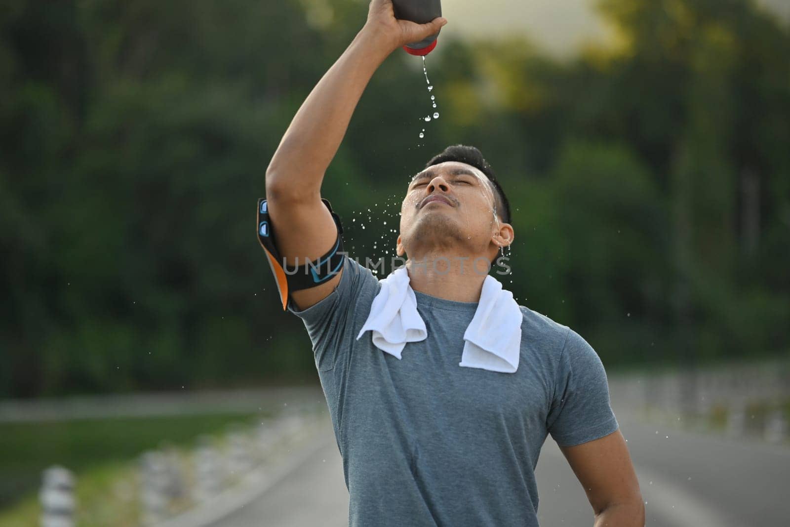 Sporty man pouring water over his face to refresh after after training hard outdoor by prathanchorruangsak