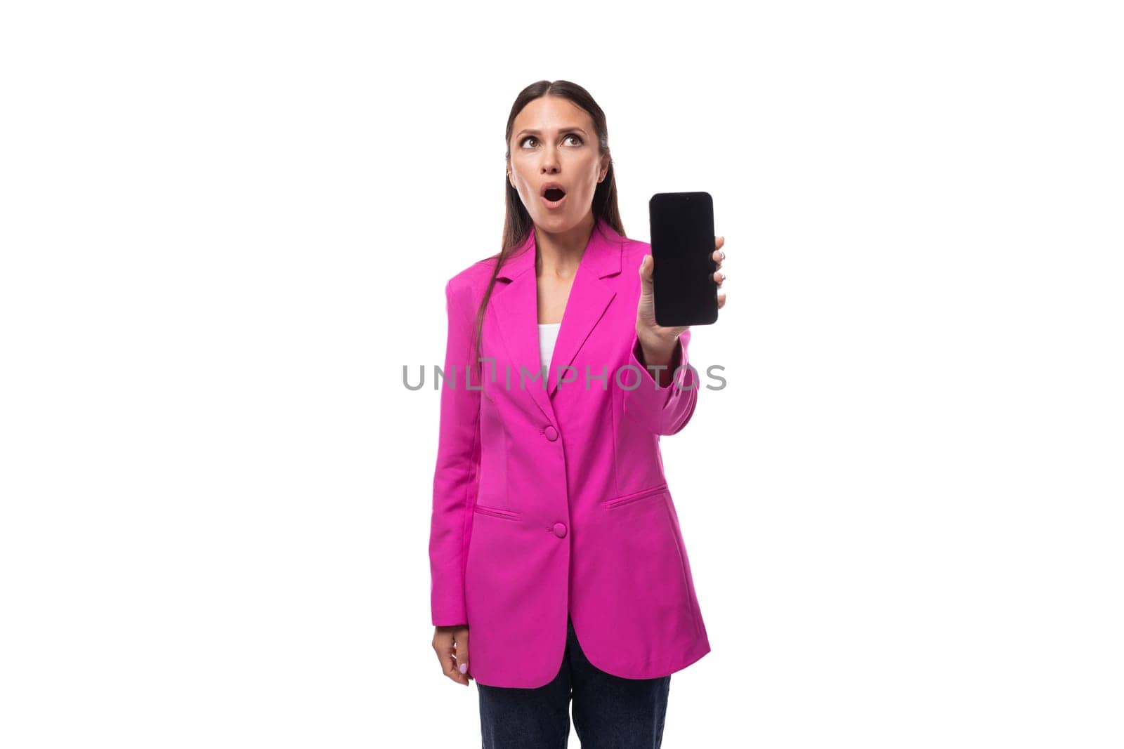 a young smart European brunette with black hair is dressed in a stylish crimson jacket with surprise showing the screen of a mobile phone by TRMK