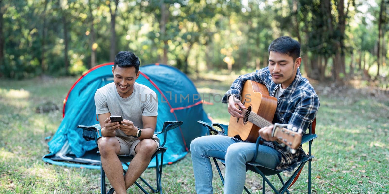 LGBTQIA Gay couple camping together in woods for holidays and relax on guitar together.