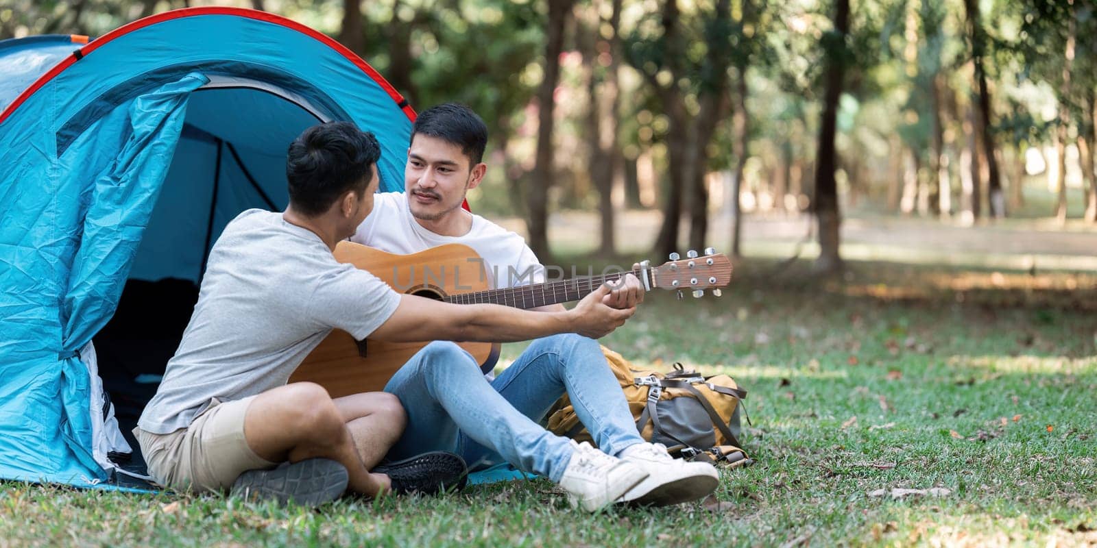 LGBTQIA Gay couple camping together in woods for holidays and relax on guitar together by itchaznong