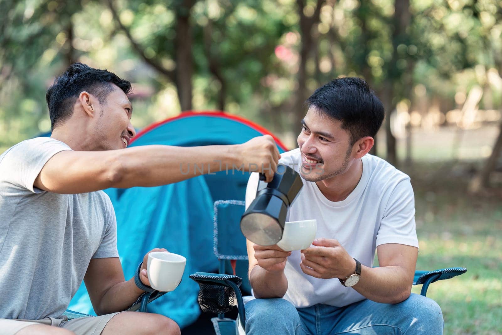Gay LGBTQIA couple sitting on picnic chair drinking tea and coffee while camping on vacation holiday by itchaznong