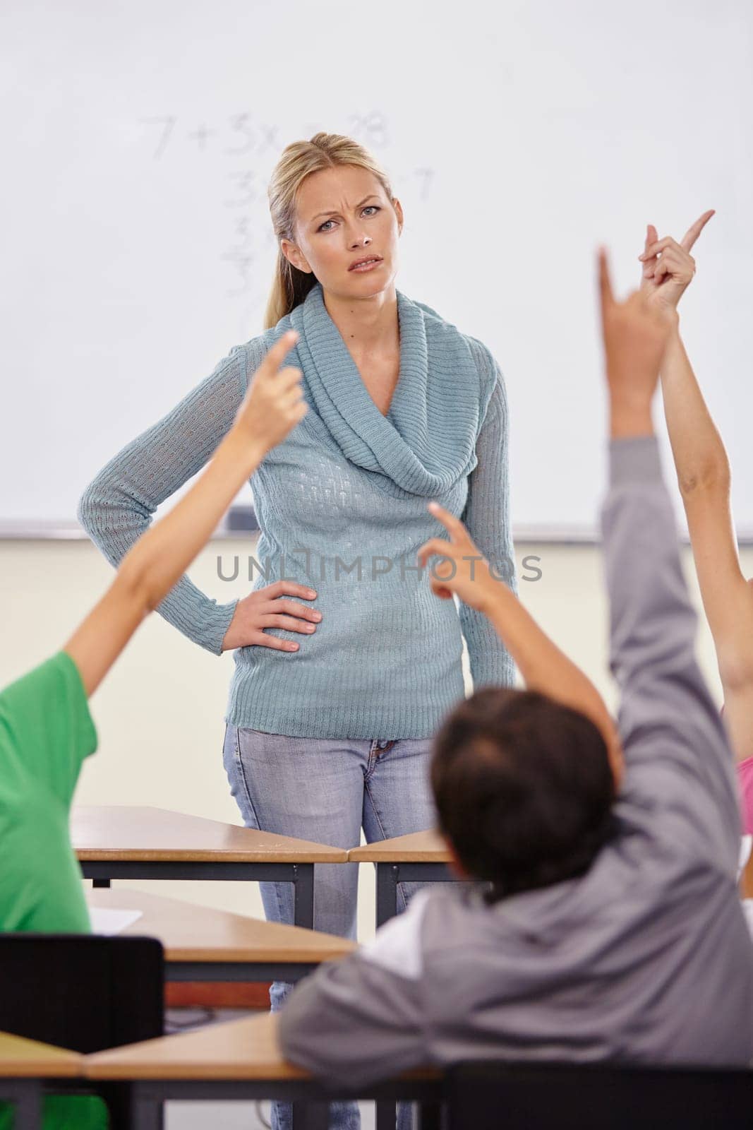 Teacher woman, children group and raised hand in classroom for question, answer or pop quiz with stress. Teaching person, school kids and education with frustrated face, talking or lecture at academy by YuriArcurs