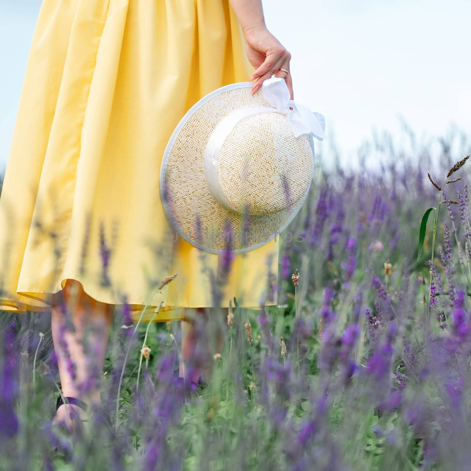 A girl in a yellow dress walks in a lavender field, a young girl between lavender bushes.