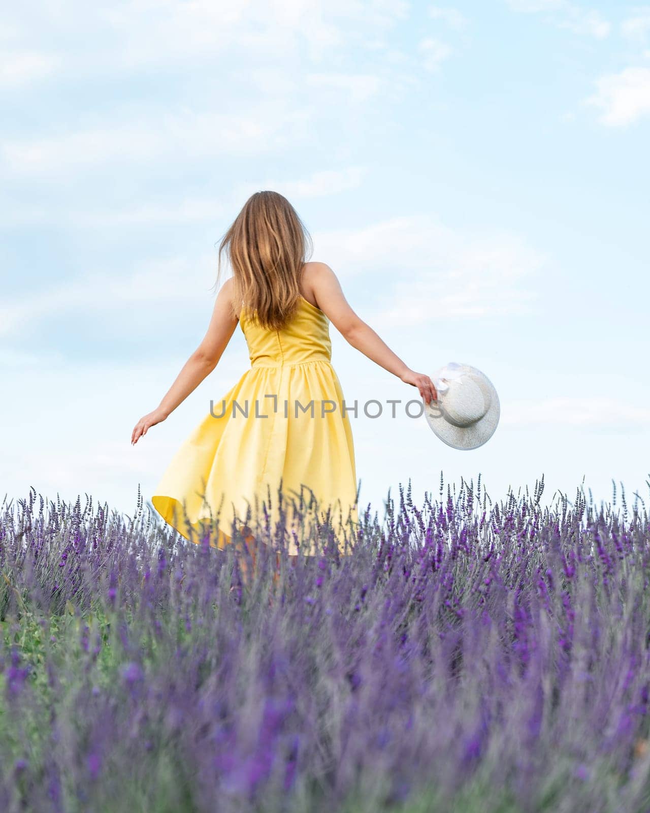A girl in a yellow dress walks in a lavender field, a young girl between lavender bushes.
