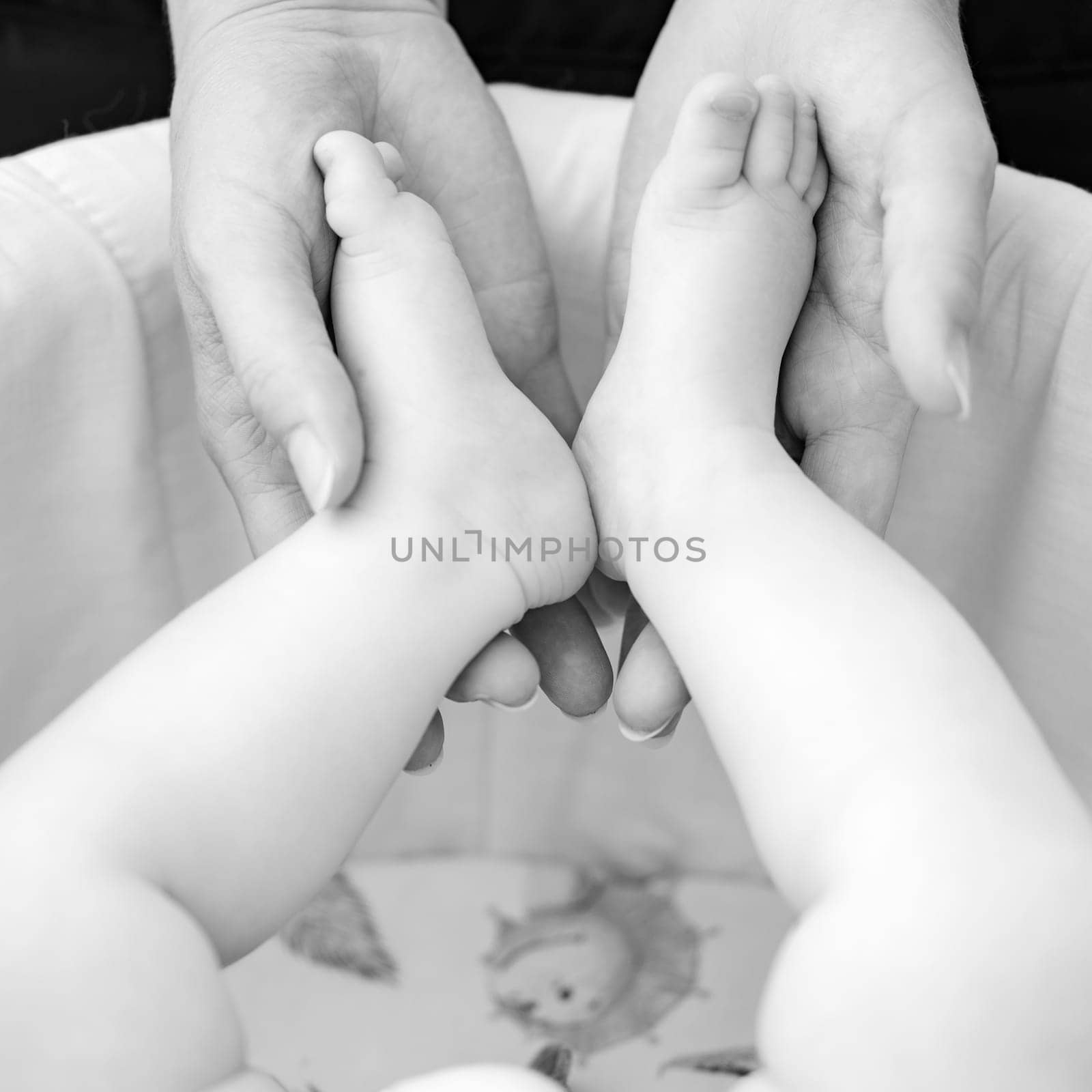 A mother holds the small legs of her newborn baby in her hands. by Niko_Cingaryuk