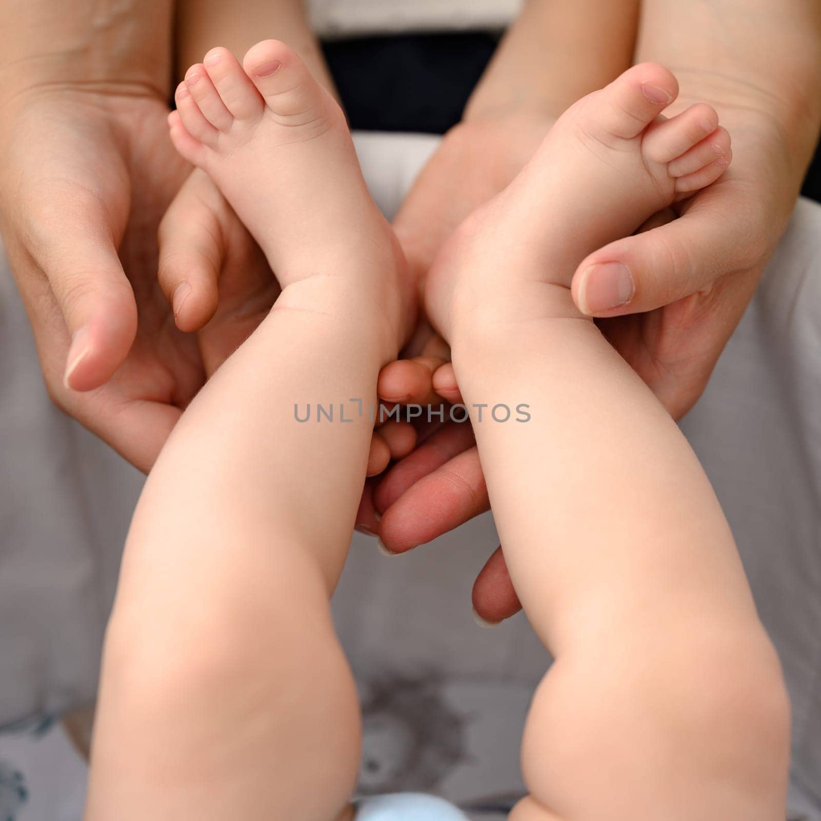 A mother holds the small legs of her newborn baby in her hands. by Niko_Cingaryuk