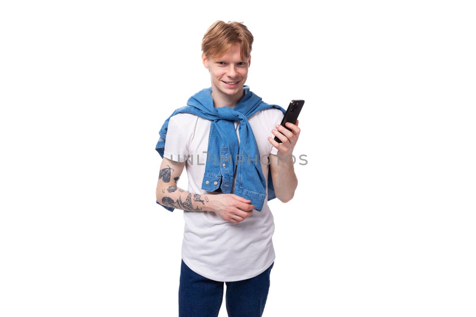 young friendly handsome european man with red hair and a tattoo on his arms writes a message on the phone by TRMK