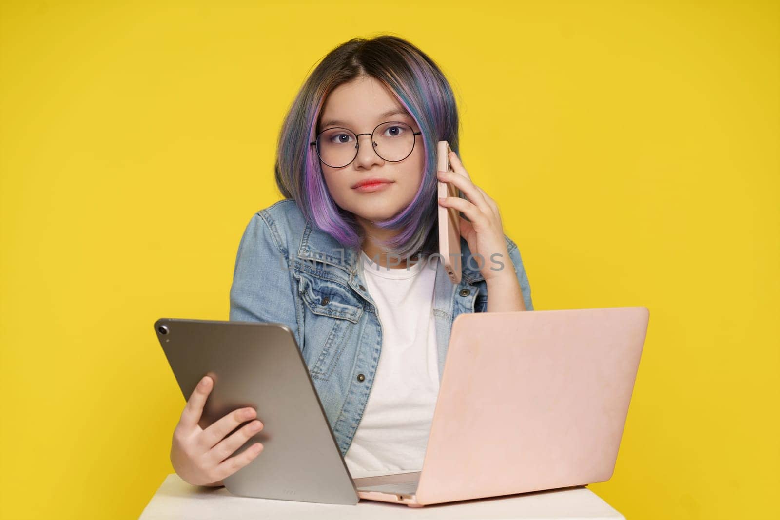 Modern Technology In Daily Life, Teenage Girl Holding Laptop, Tablet Pc, And Mobile Phone. Isolated On Yellow Background, Concept Of Tech-Savvy Lifestyle, Devices Seamlessly Integrate Into Daily Activities. by LipikStockMedia