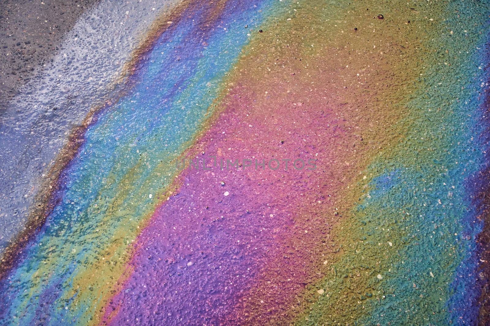 Multi-colored poisonous spots of spilled gasoline on wet pavement during rain. Rain blurred the car oil from a malfunctioning car in a parking lot
