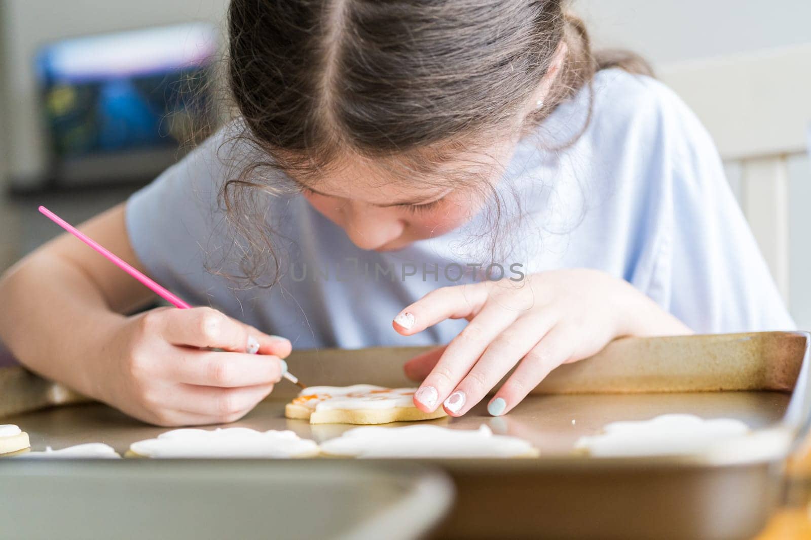 A heartwarming scene of a little girl carefully writing 'Sorry' on sugar cookies with food coloring, the cookies beautifully flooded with white royal icing.