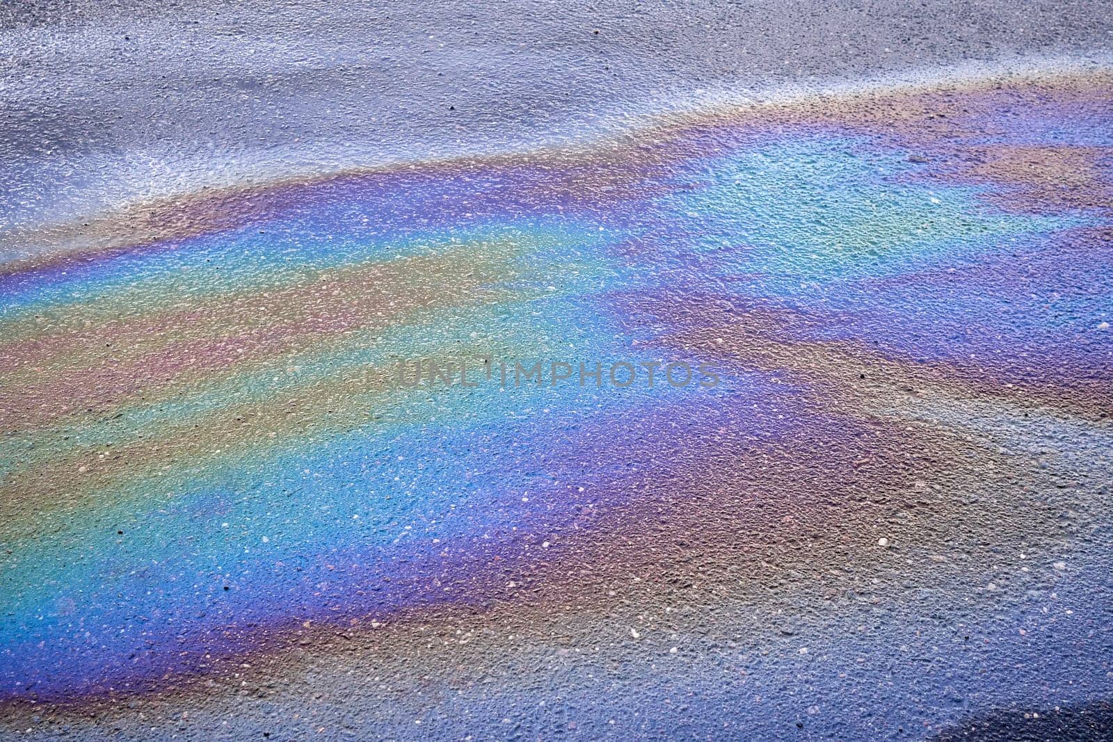 Background texture of an oil spill in the form of a rainbow stain on dark asphalt, parking..