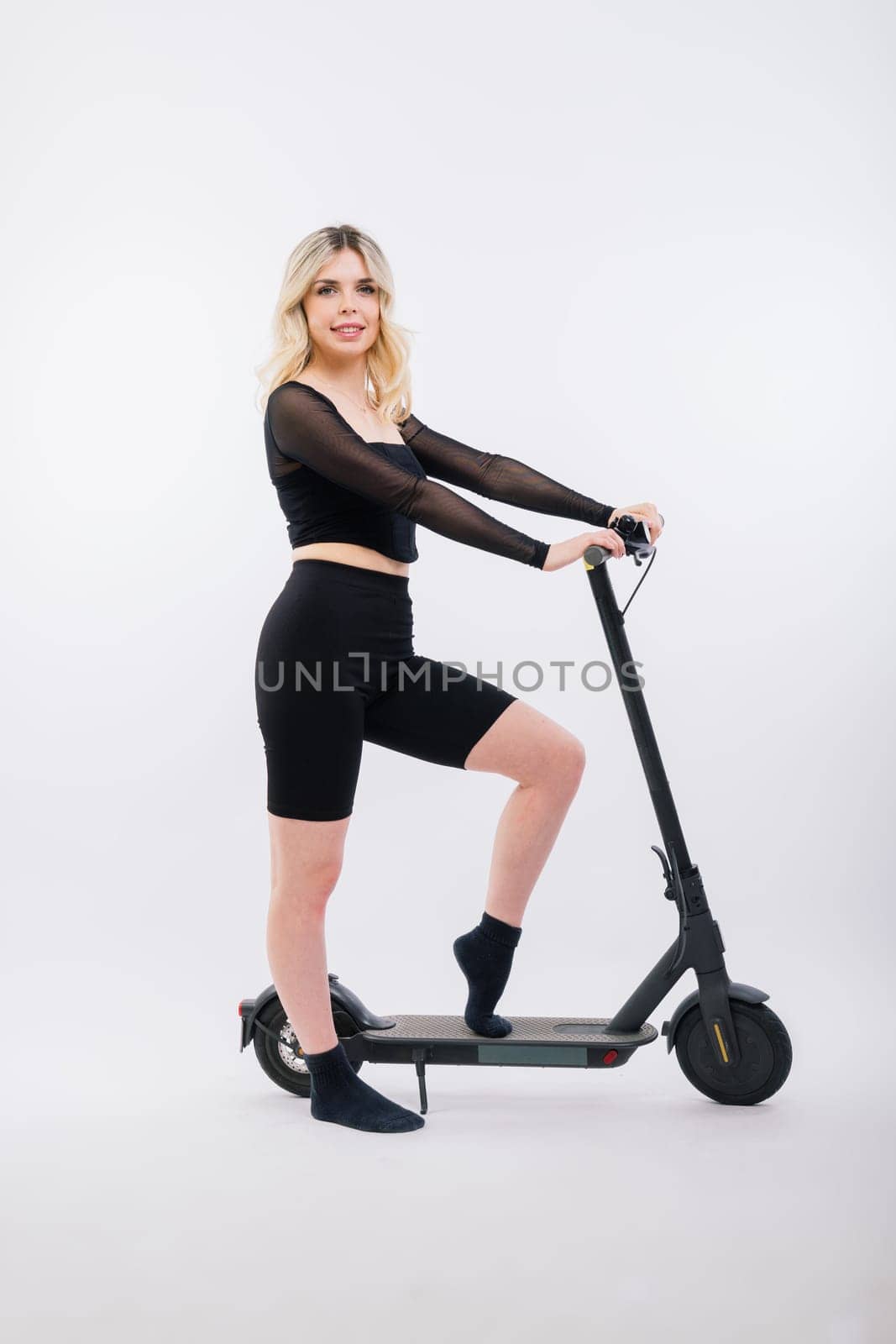 Female in a sport clothes stands on electric scooter with sunglasses on red and white background