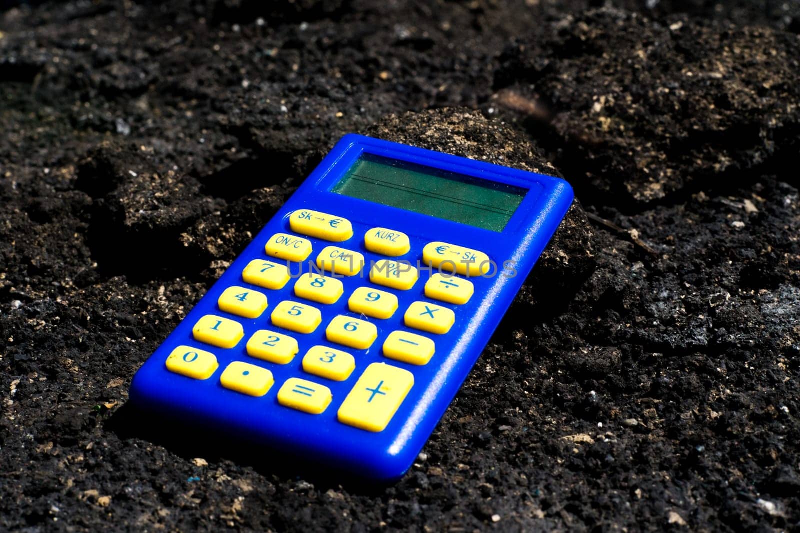 Blue calculator in dark soil, burnt ground after a fire