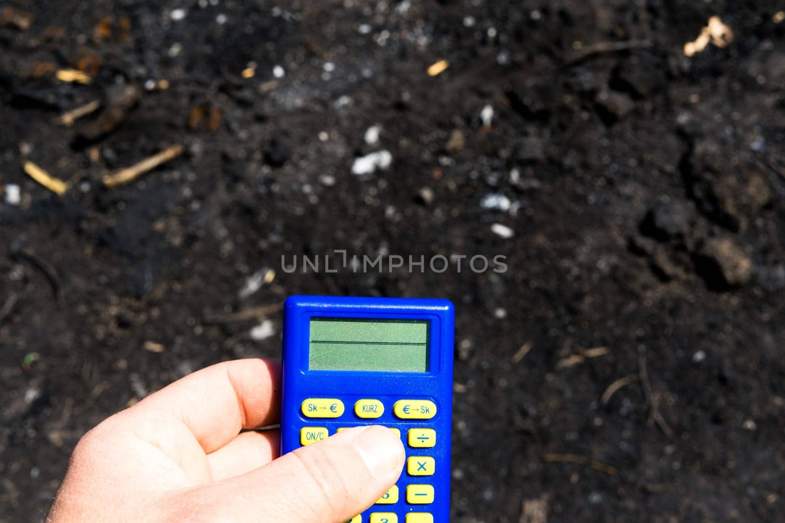 Blue calculator in dark soil, burnt ground after a fire
