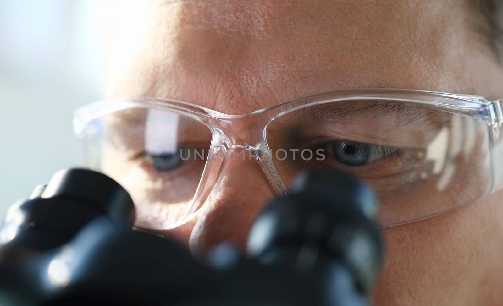 Handsome man scientist looking through binocular microscope examining diseases of the virus that infects water vivo ivf