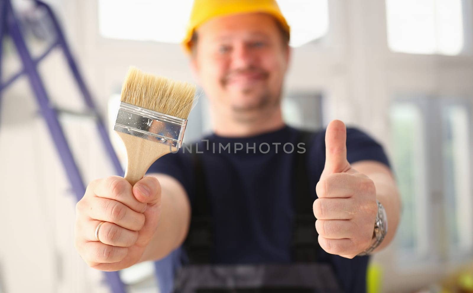 Arms of worker hold paint brush and show confirm sign with thumb up closeup. Manual job DIY inspiration joinery startup idea fix shop hard hat industrial education profession career concept
