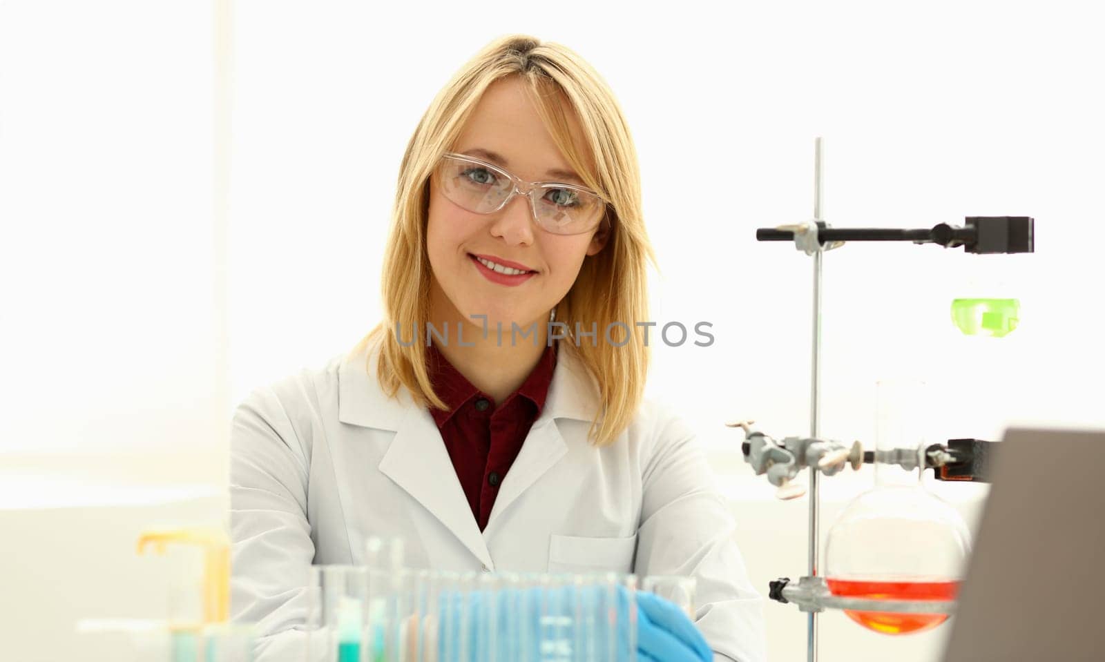 Smiling beautiful technician woman portrait and sample bottle with poison fluid. Medical worker in uniform use reagent tube for virus infection exam or biological toxic reaction, drug creation