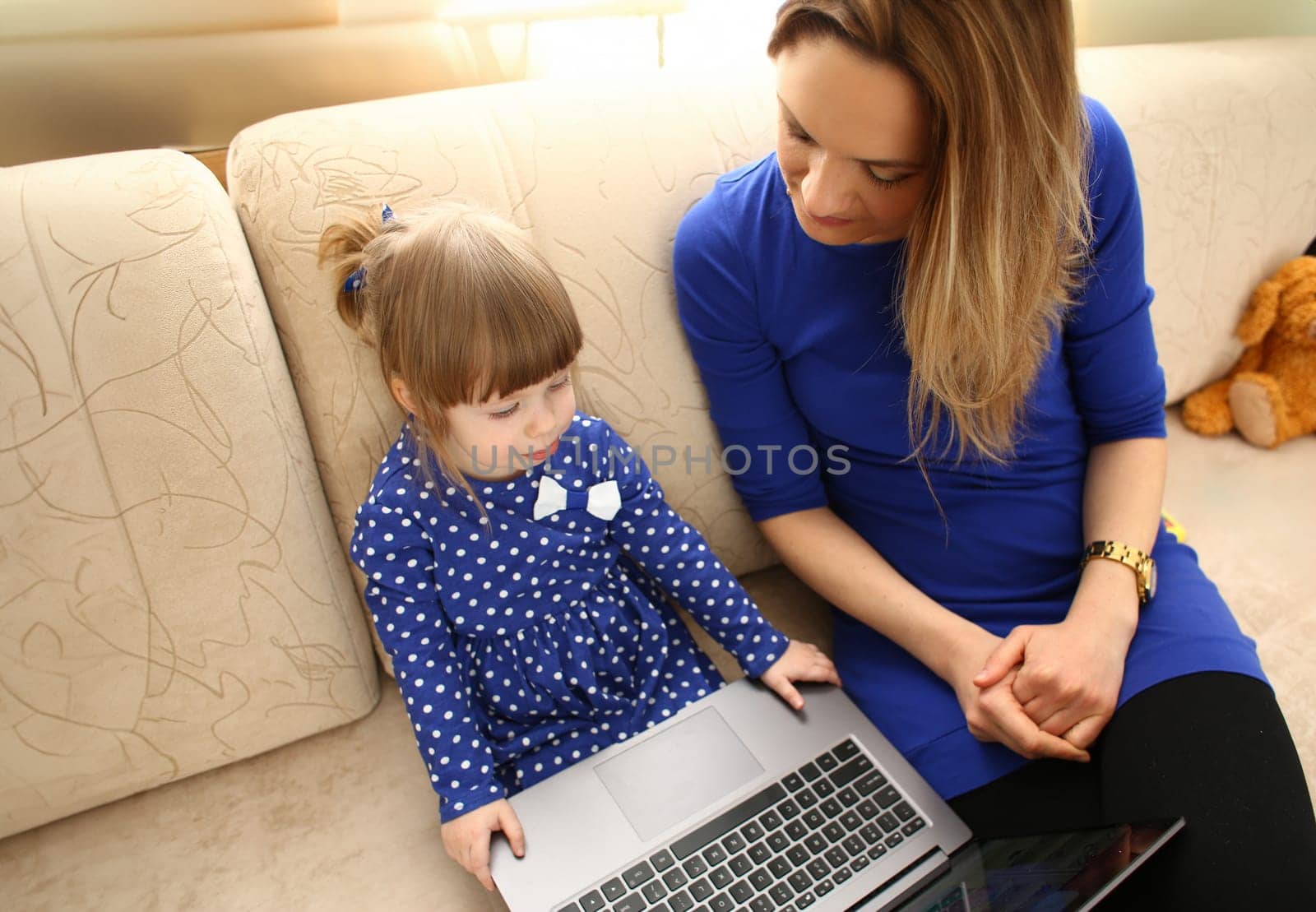 Cute little girl on couch with mom use laptop pc for chat with her dad away on business portrait. Point finger hand in display social web network bank mortgage credit wireless ip telephony concept