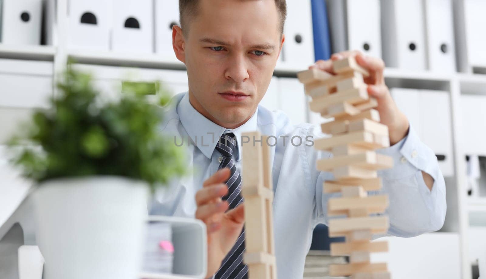 Businessman plays in strategy hand rearranging wooden blocks involved during break at work in office sitting table gaming pile fun joy pastime concept
