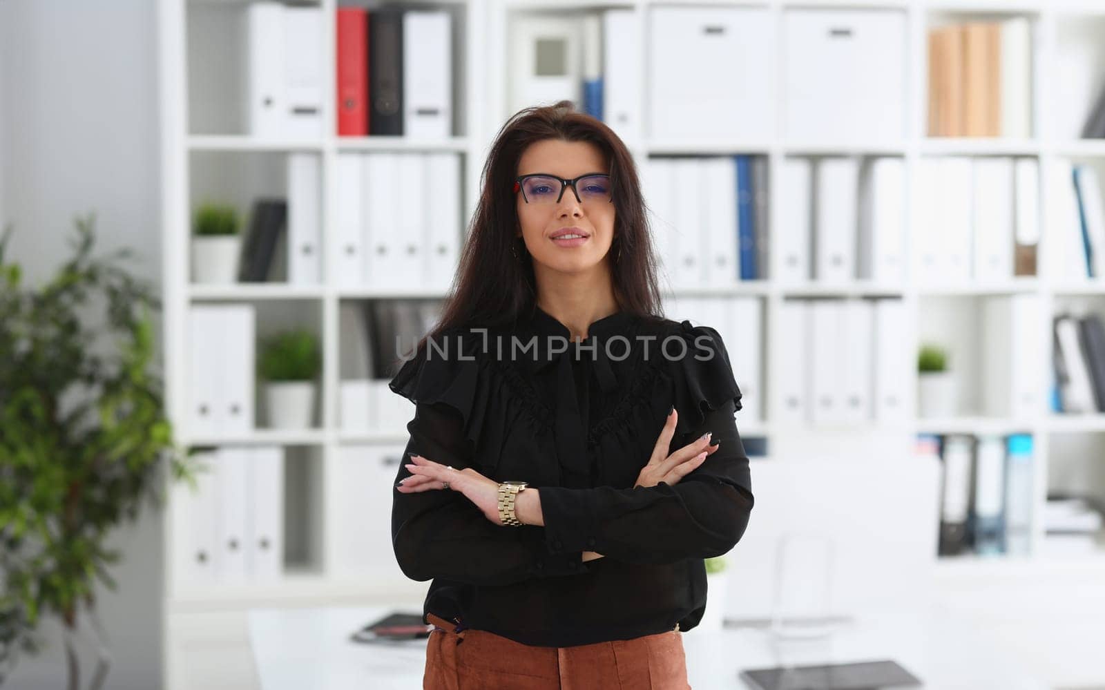 Beautiful smiling brunette woman in office posing arms crossed on chest wearing stylish glasses portrait. White collar worker at workspace officer highly pay smart serious job offer headhunter hr