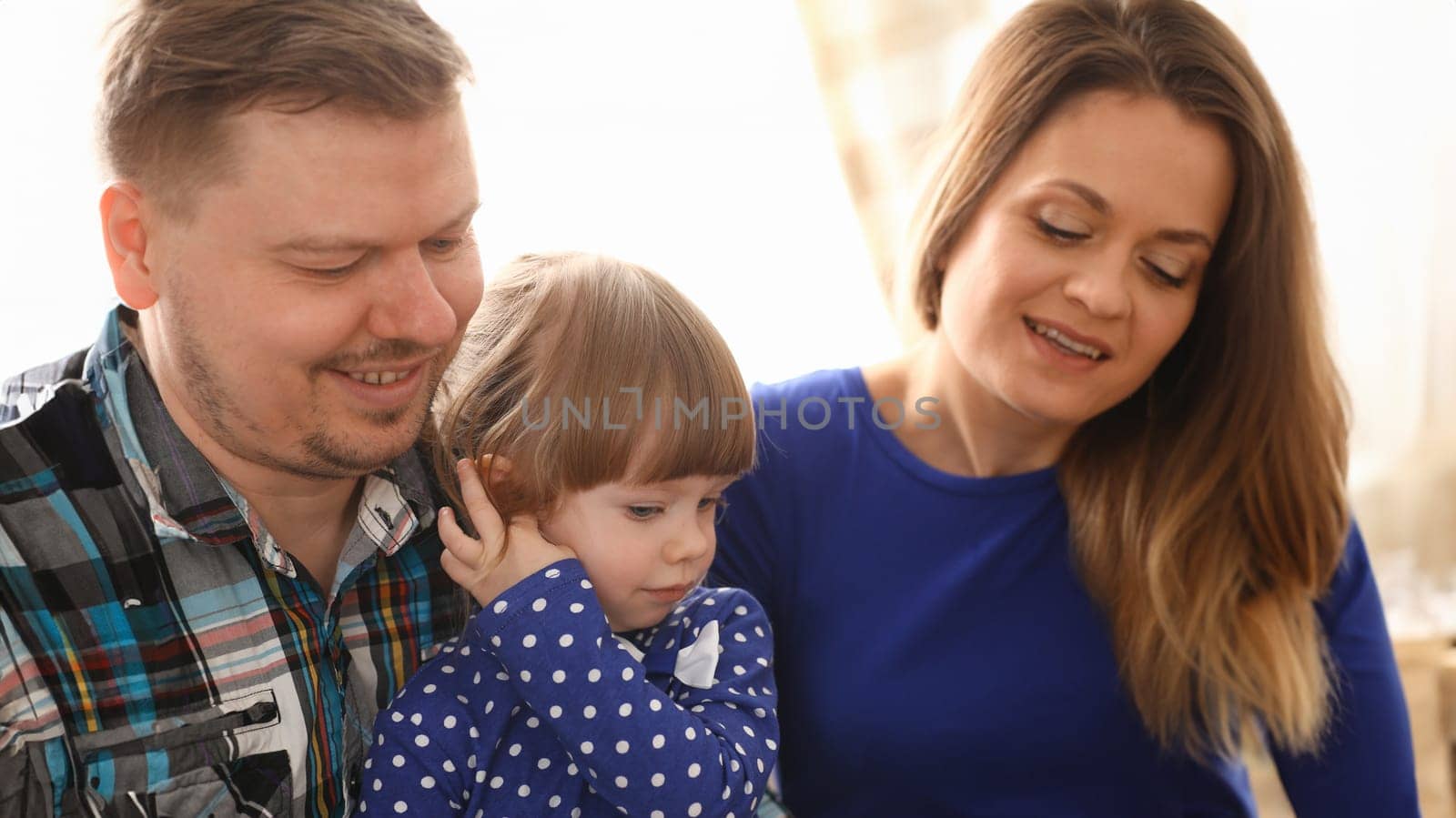Happy parents with daughter at sofa at home. Beautiful smiling woman and handsome man play with cute little girl childhood and parenthood concept
