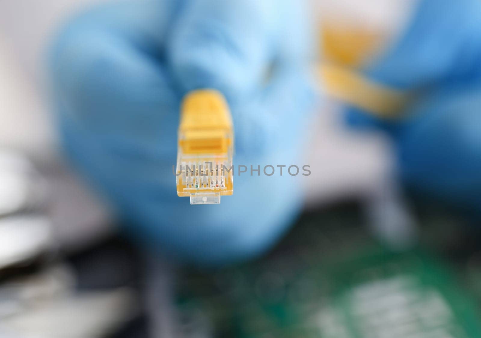 A male hand in blue protective gloves holds a network connector. The LAN constructor deconstructs the connection of clients to the Internet on the basis of xpon and Adsl