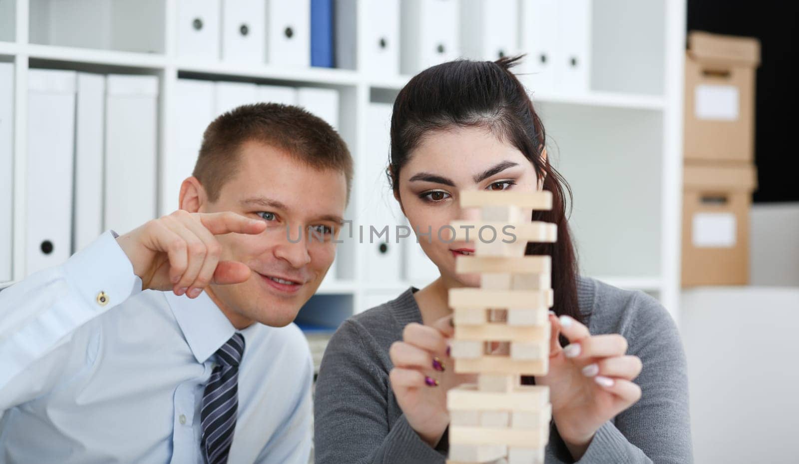 Businessman and businesswoman plays in strategy hand rearranging wooden blocks involved during break at work in office sitting table gaming pile fun joy pastime concept.