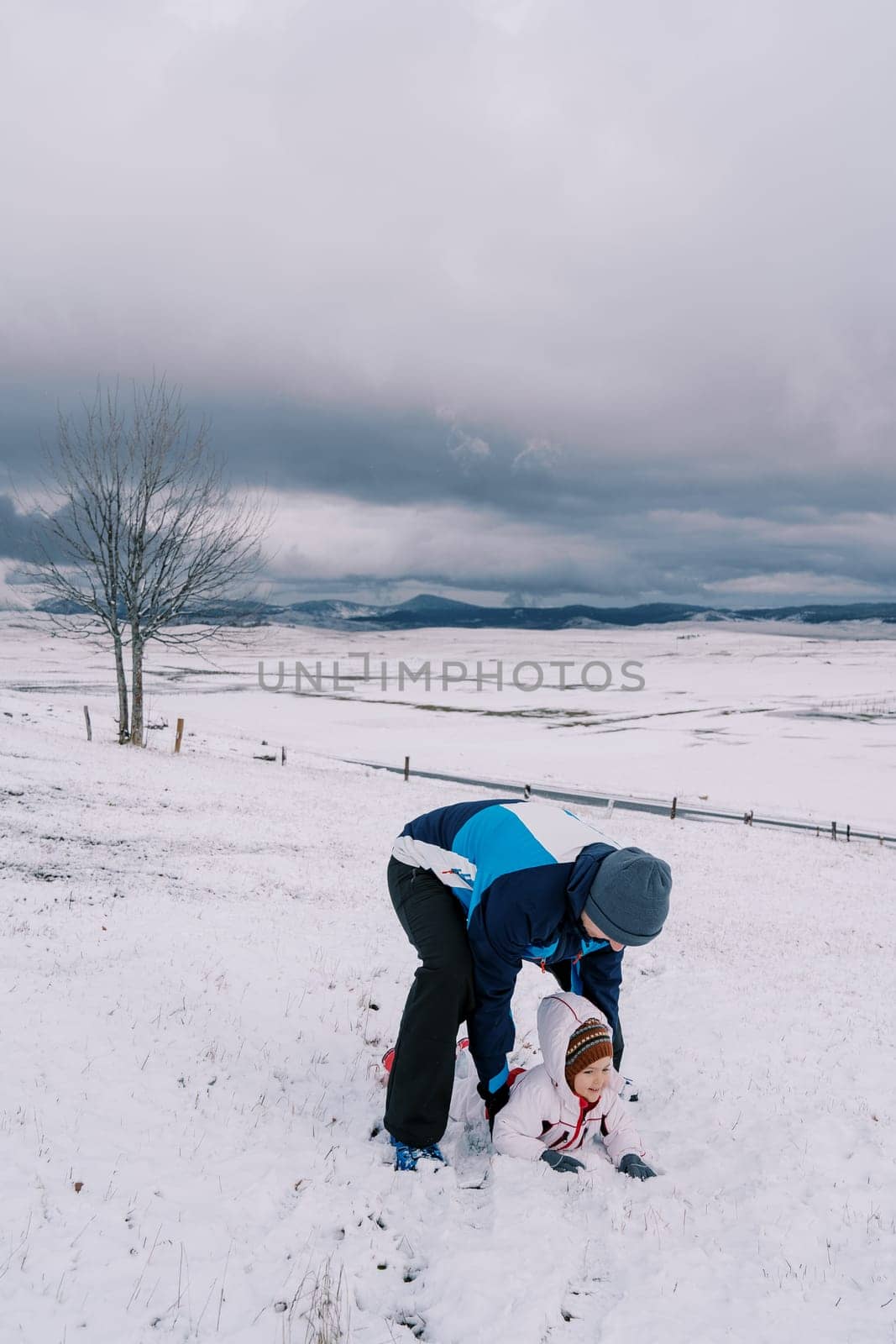 Dad leaned over the little girl lying on her stomach in the snow and lifted her. High quality photo