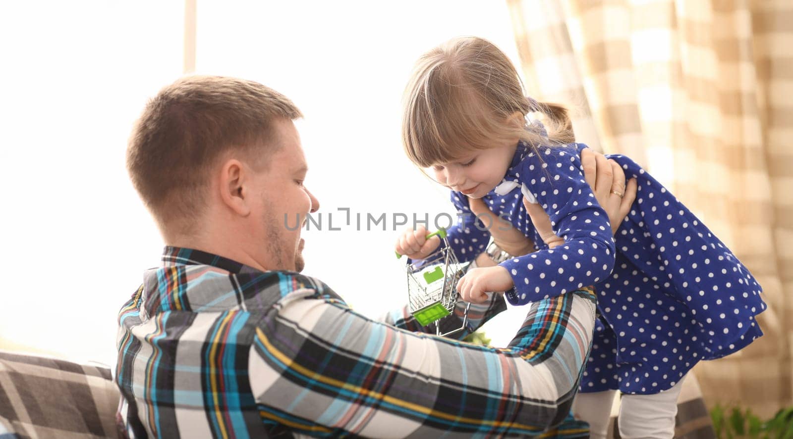 Dad play with cute little girl in blue dress on couch at home portrait