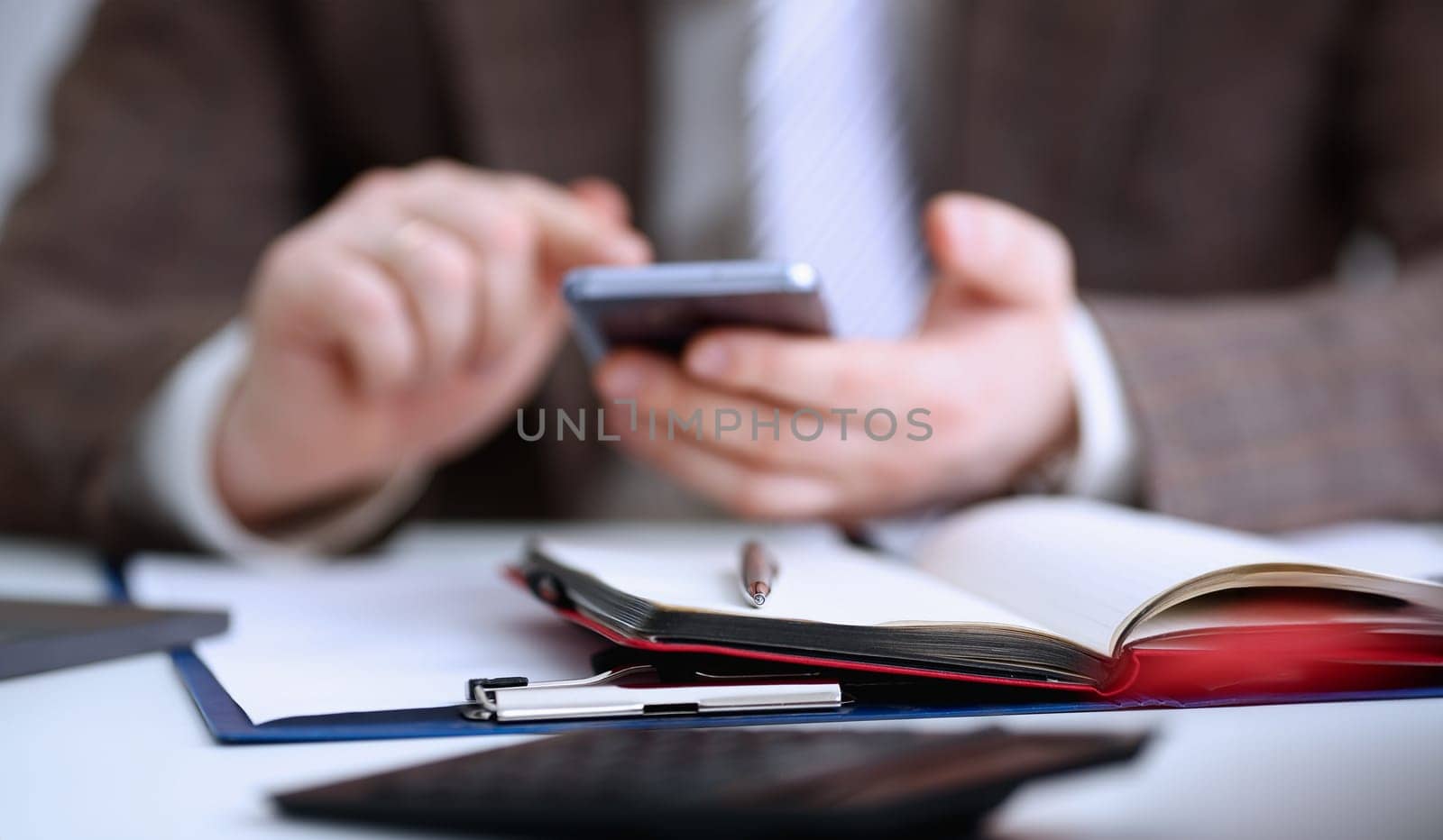 Male arm in suit hold phone and silver pen at workplace closeup. Read news mania send sms chat addict use electronic bank modern lifestyle job plan colleague share blog tweet web application search