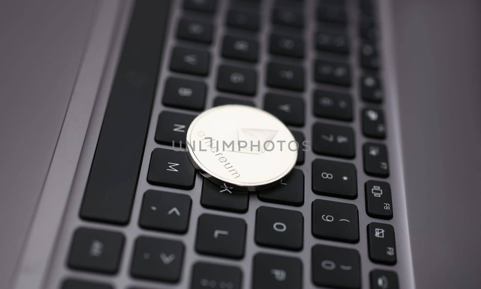 Silver ethereum coin is lying on laptop by kuprevich