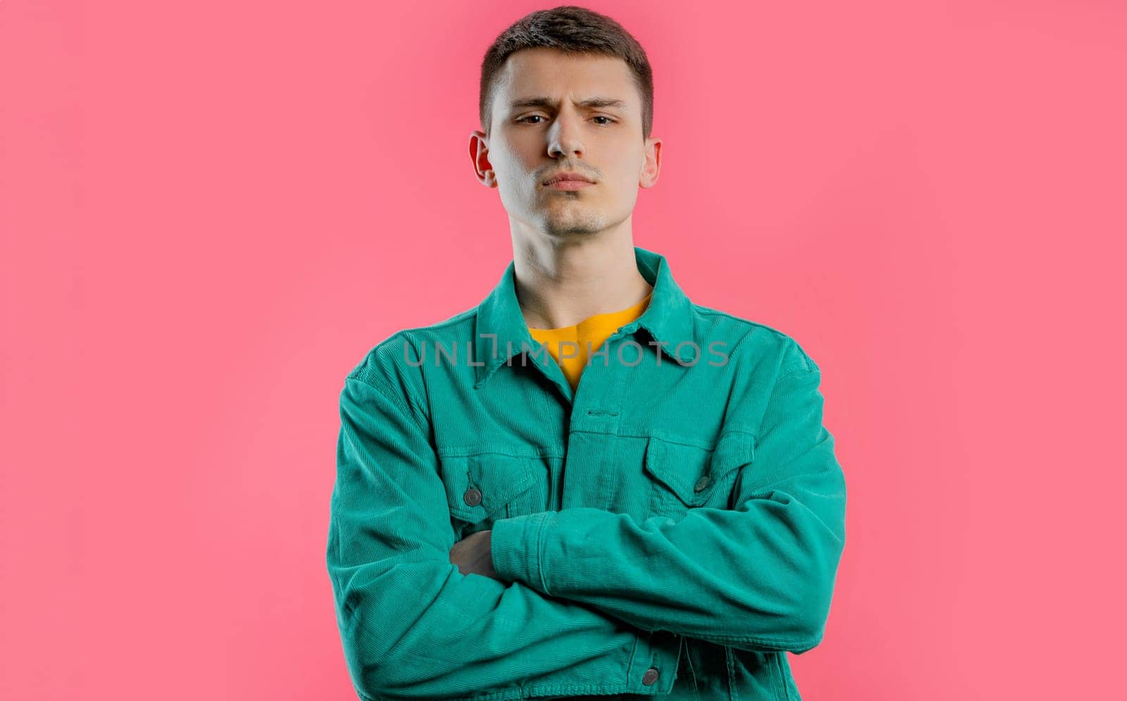 Offended young man, arms crossed, feeling mad. Teen maximalism. Pink background. by kristina_kokhanova