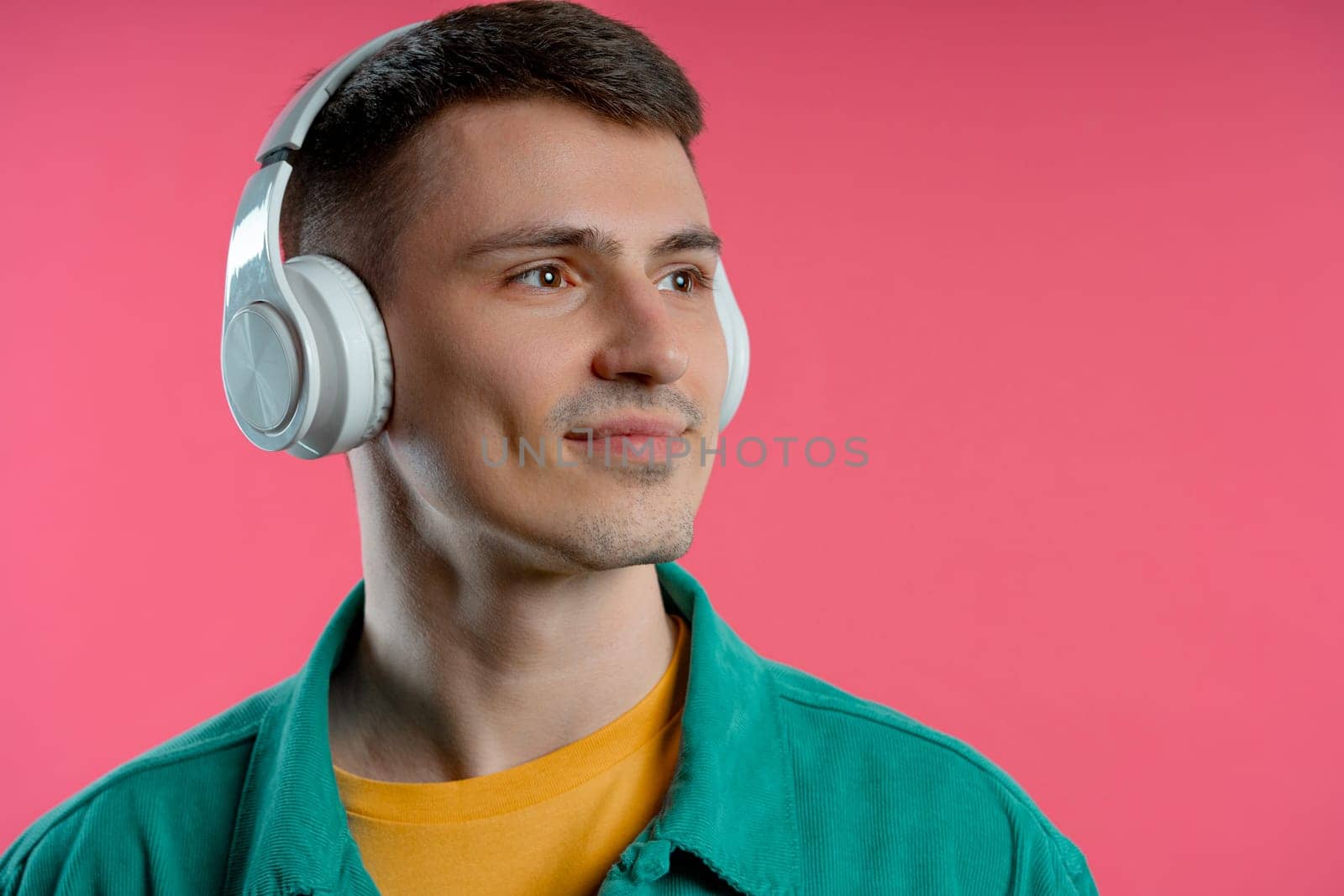 Positive man listening music, enjoying dance with headphones on pink studio by kristina_kokhanova