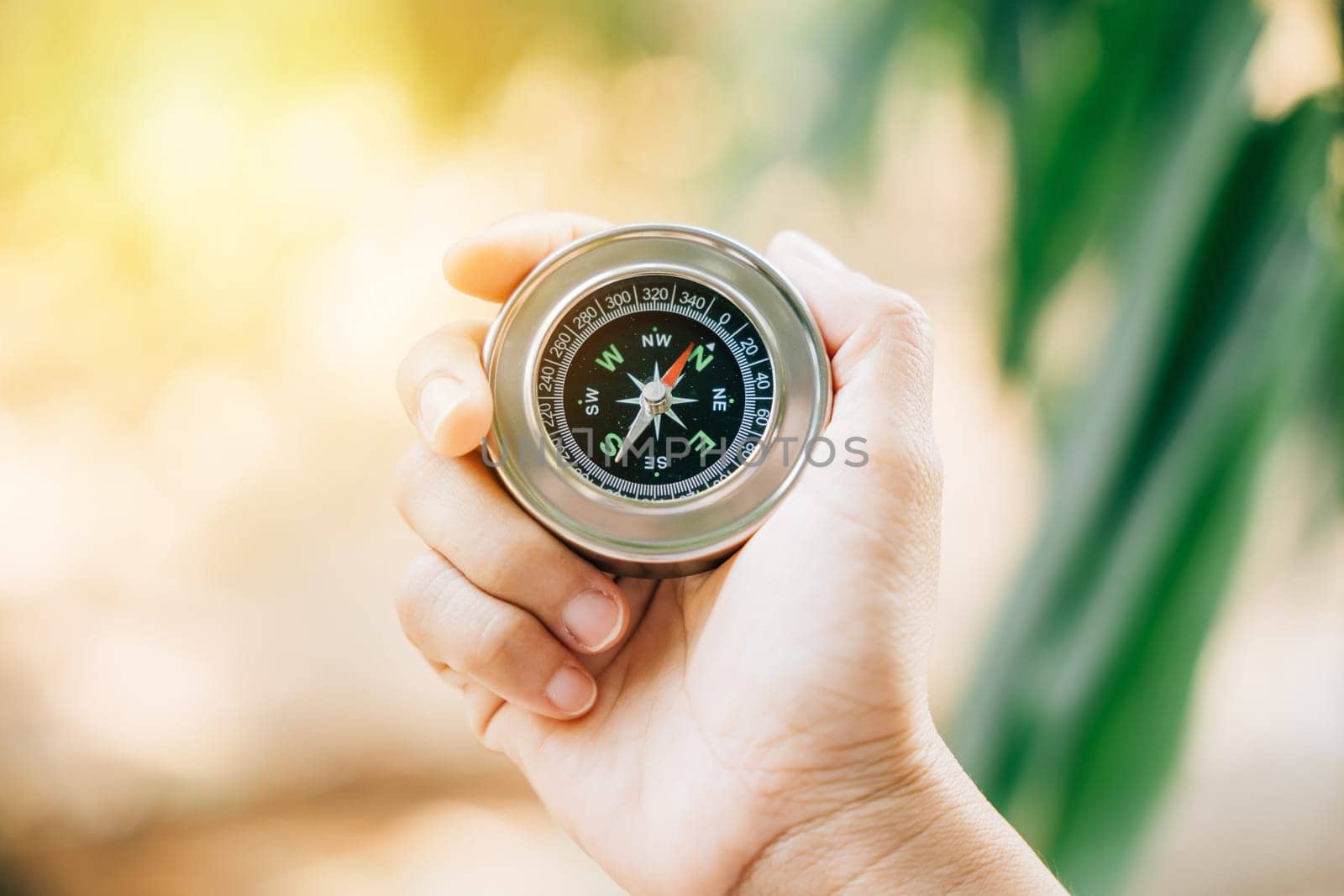 Traveler holds a compass in a park finding her way amidst confusion. The compass in her hand symbolizes guidance exploration and the journey to conquer defeat. by Sorapop