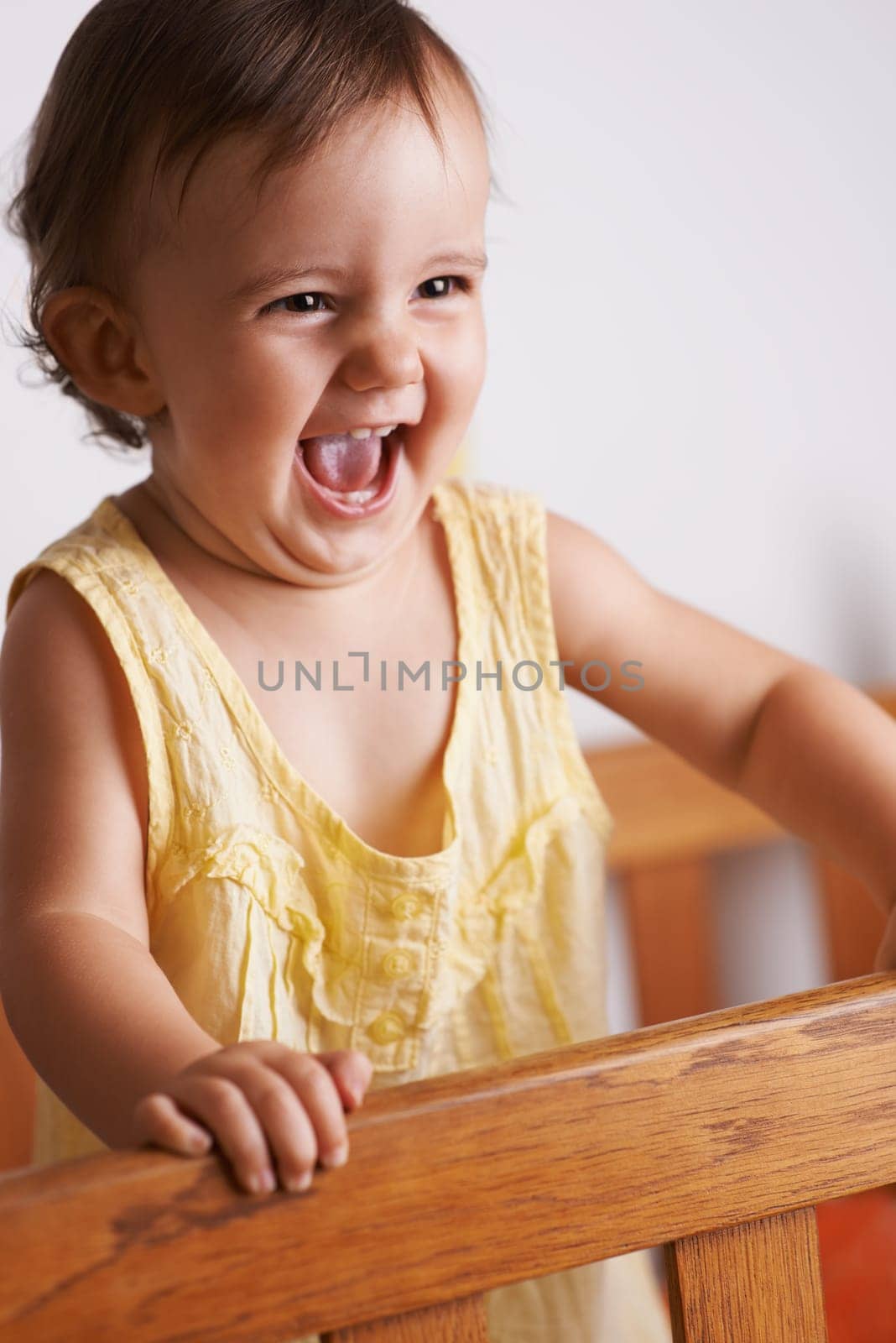 Cute, happy and a child in a crib for playing, wake up or comfort in a bedroom. Laughing, baby and a young kid in a nursery or room for thinking, idea or innocent standing for development in a home.