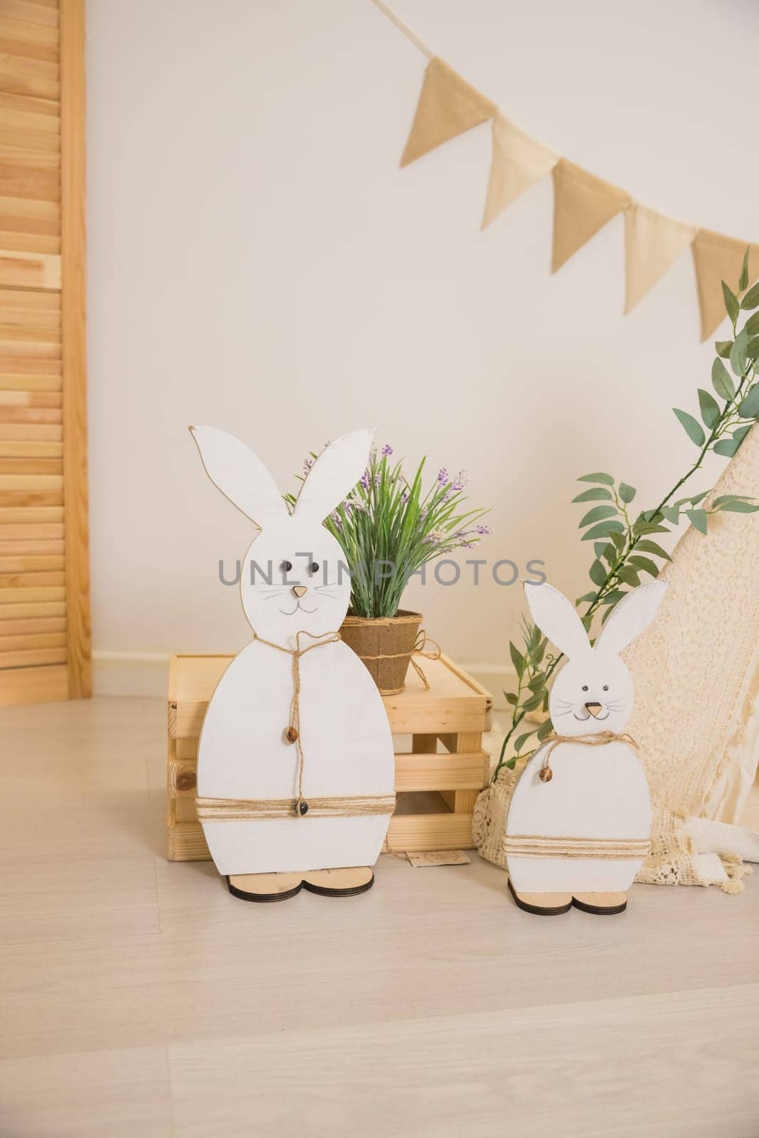 Interior design of easter living room with easter bunny sculptures, garland, plants, wooden boxes,beige wall with stucco. Home decor.Warm and cozy composition by YuliaYaspe1979