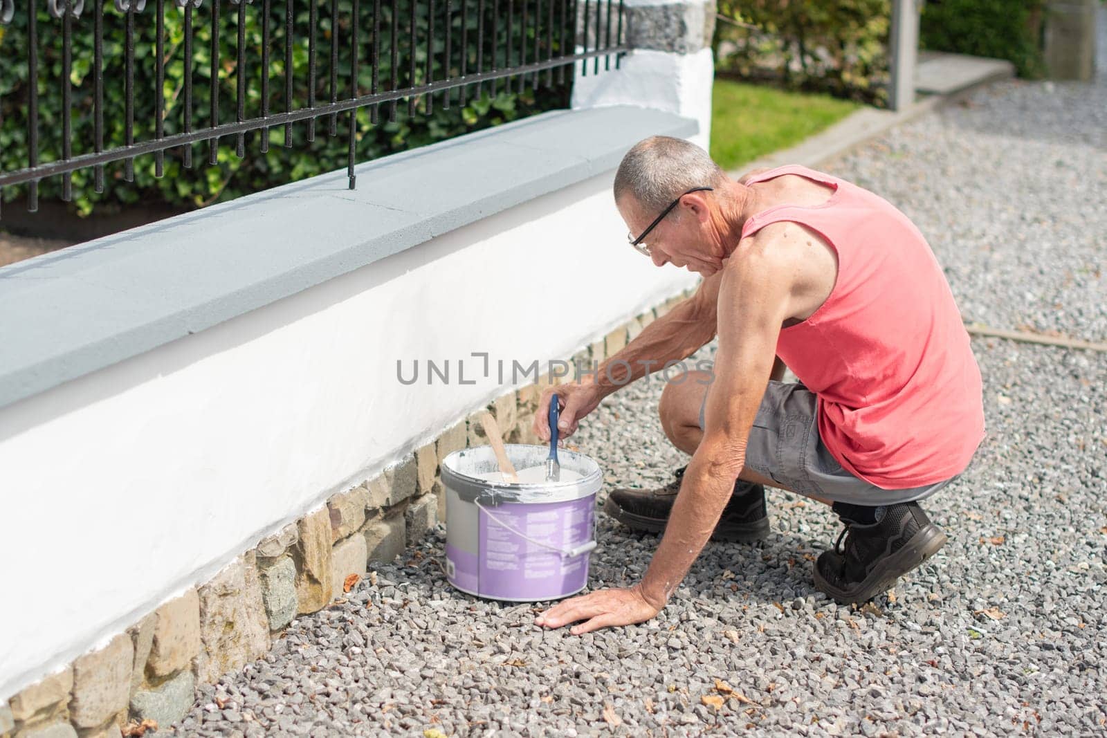 A middle-aged man paints a fence with white paint with a brush, repairs the damaged surface, High quality photo