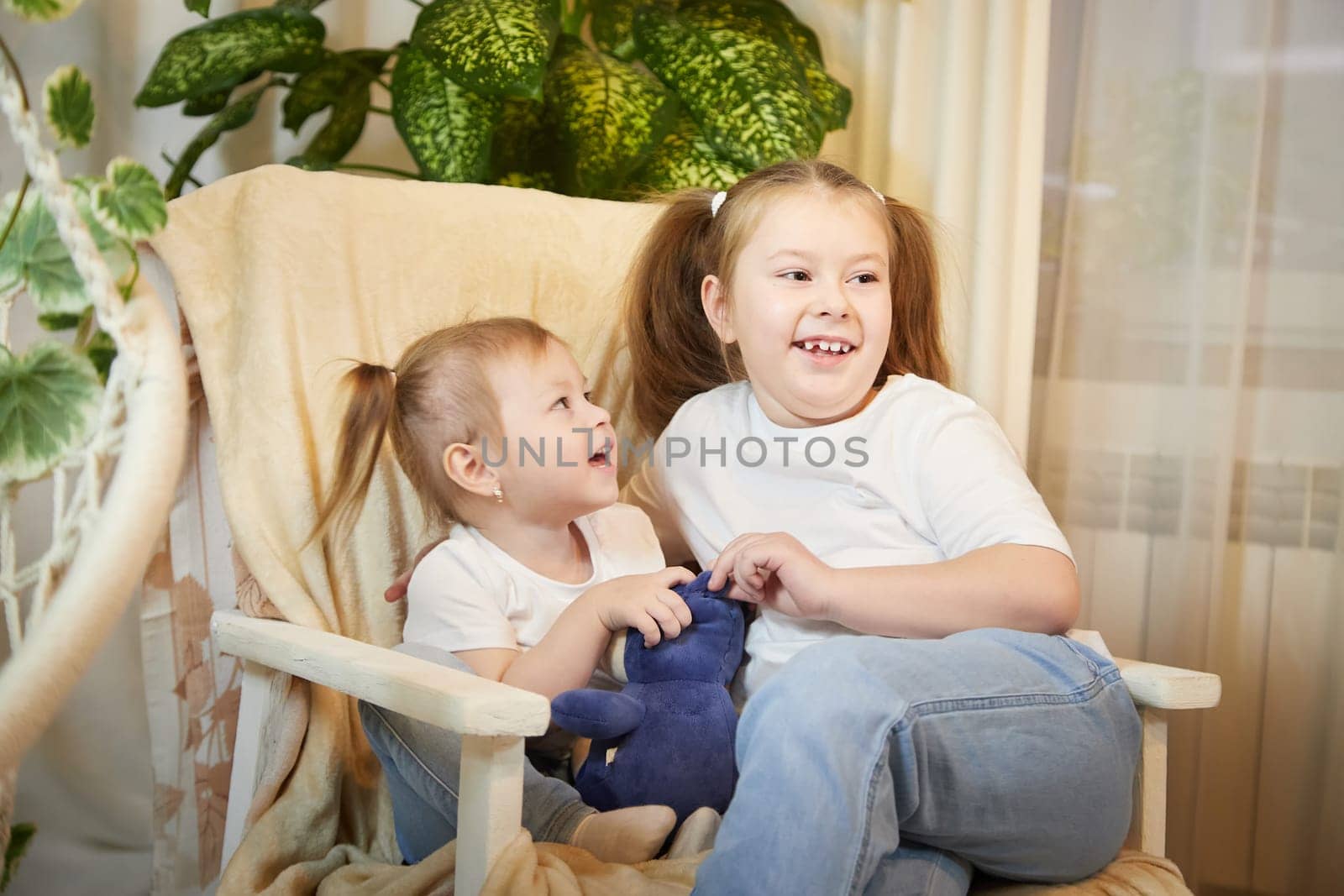 Happy time concept. Girls Sisters in chair and having fun. Female Preschooler and teenager playing and relaxing in room