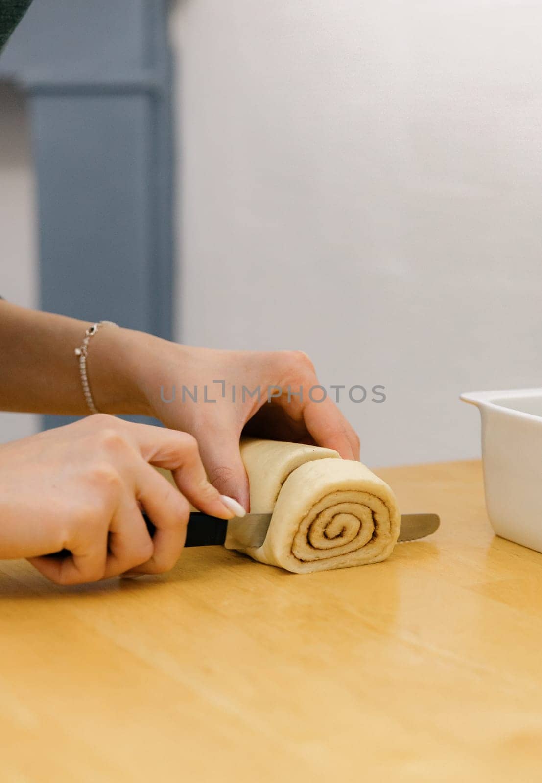 One unrecognizable young Caucasian girl cuts dough with brown sugar with cinnamon into pieces using a knife on a wooden table, standing in the kitchen, close-up side view. Step-by-step instructions for baking synabons. Step 9.