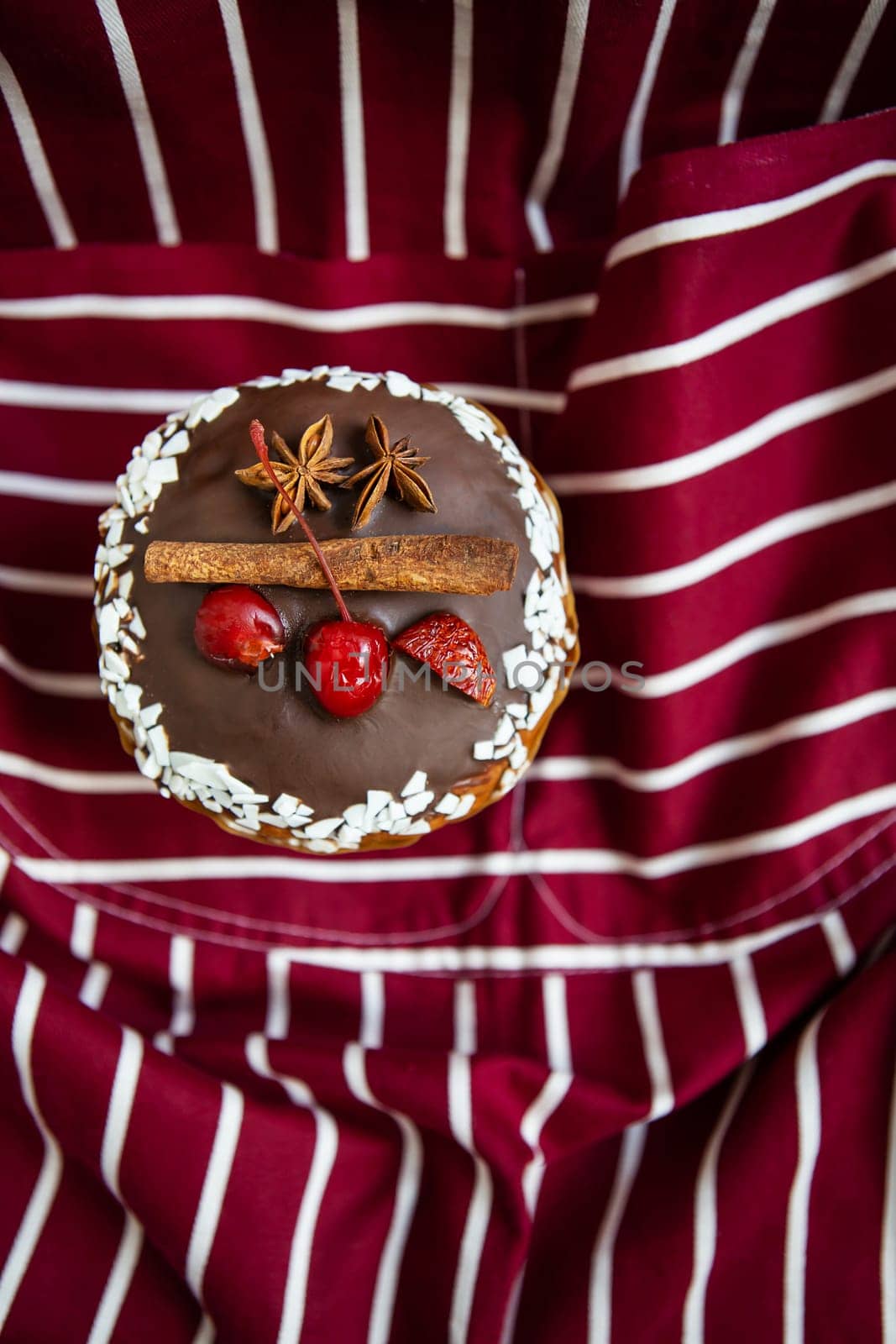 A traditional paska decorated with white and dark Swiss chocolate and cherries, cinnamon and star anise stands on a cherry striped apron. Easter holiday, top view