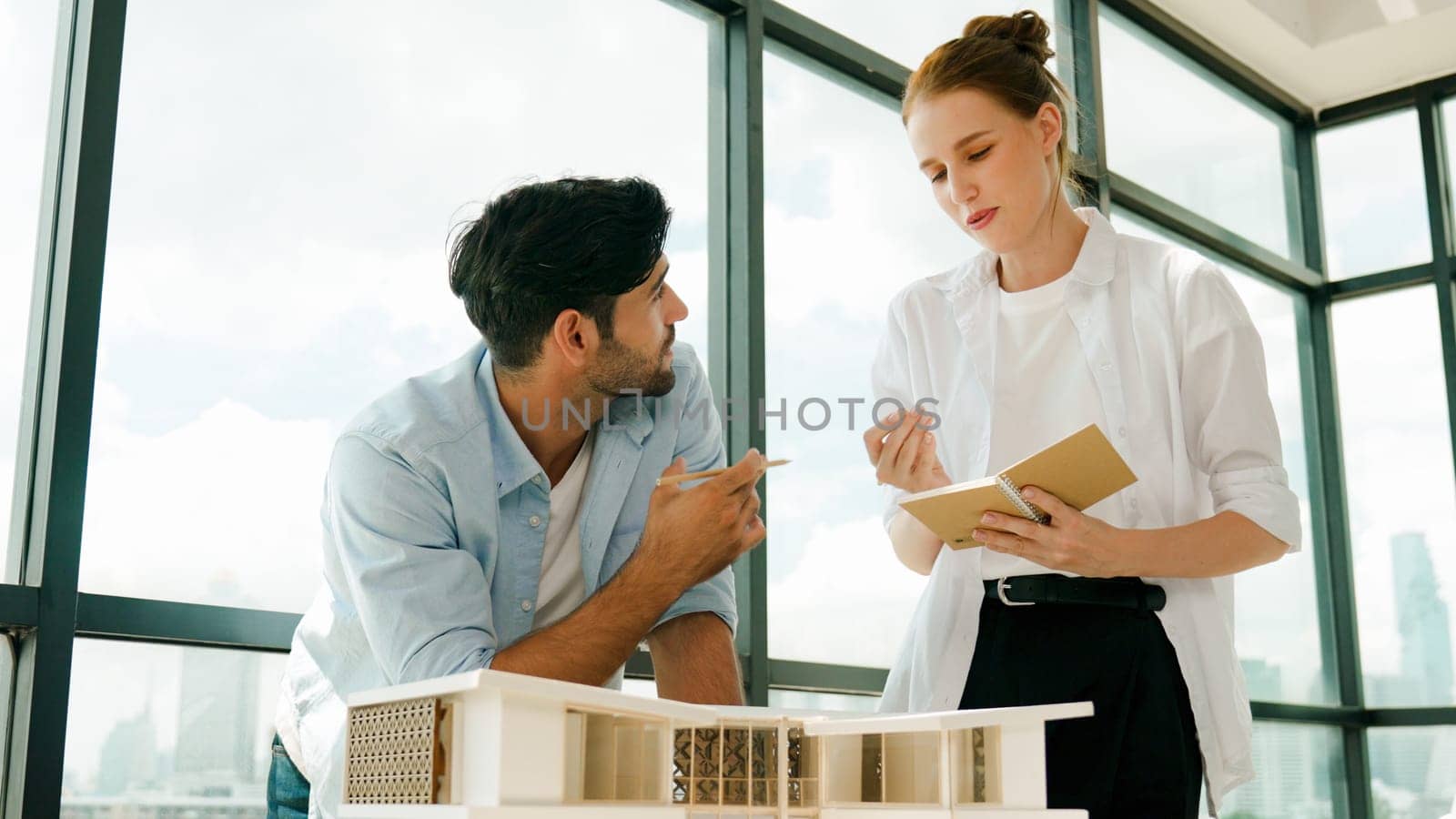 Skilled architect engineer team discussion about house model construction. Smart interior designer sharing, talking about building design while beautiful coworker taking a note. Design. Tracery