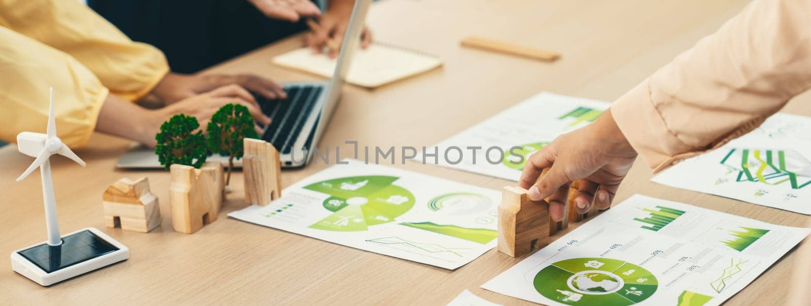 Environmental documents and a windmill model representing the use of clean energy are scattered on the table during a green business discussion about investing in clean energy. Closeup. Delineation.