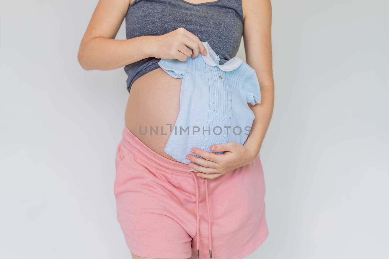 A tender moment: expectant mom cradling baby clothes against her growing belly, anticipating the joy of motherhood.