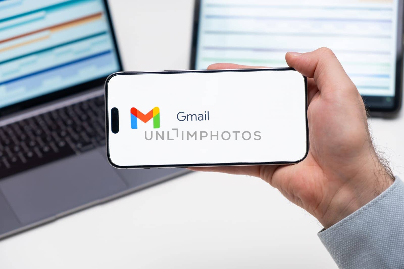 Gmail application logo on the screen of smart phone in mans hand, laptop and tablet on the table by vladimka