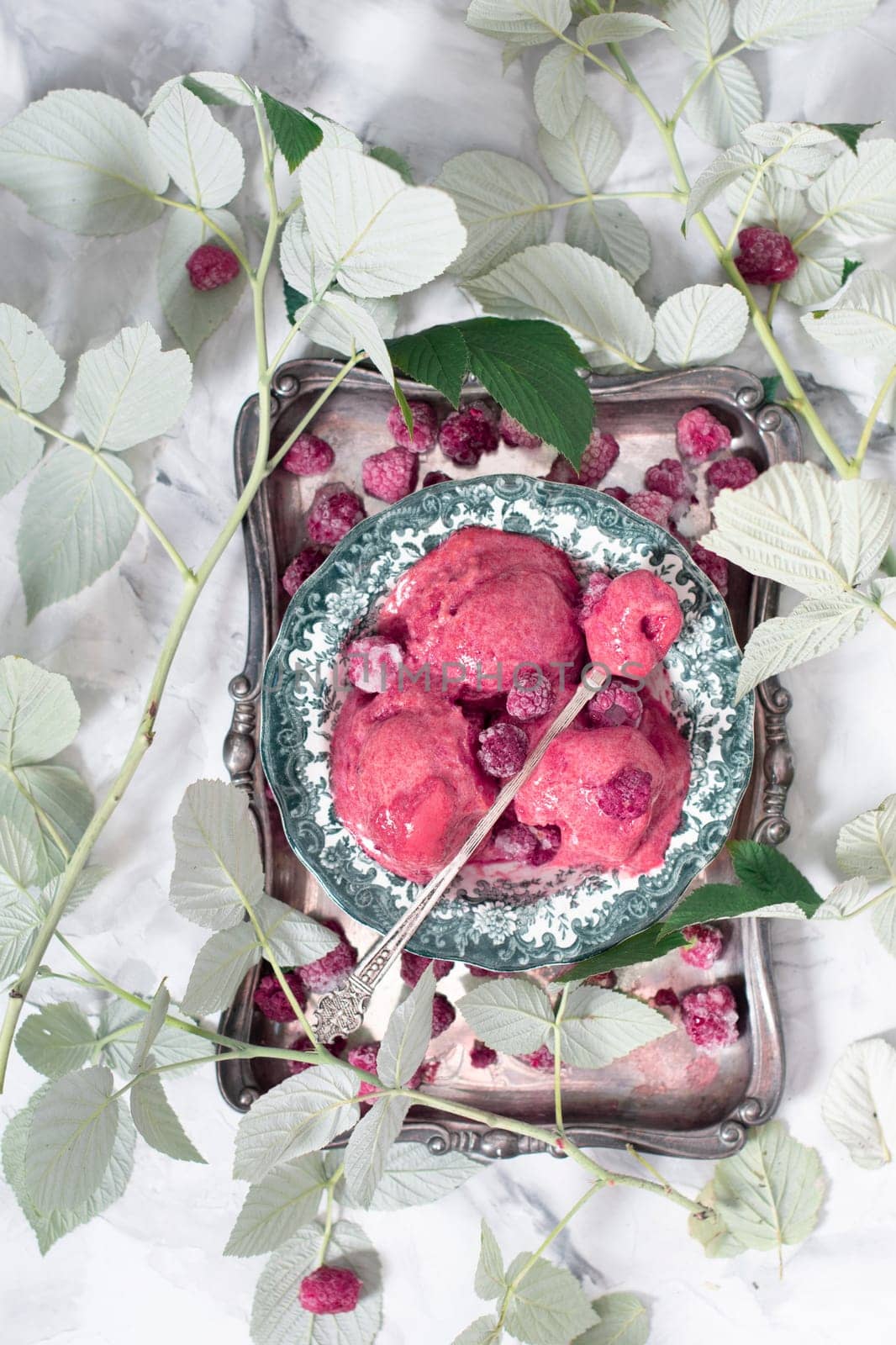 Raspberry purple ice cream sorbet on a silver plate surrounded by green leaves, summer dessert, top view. High quality photo