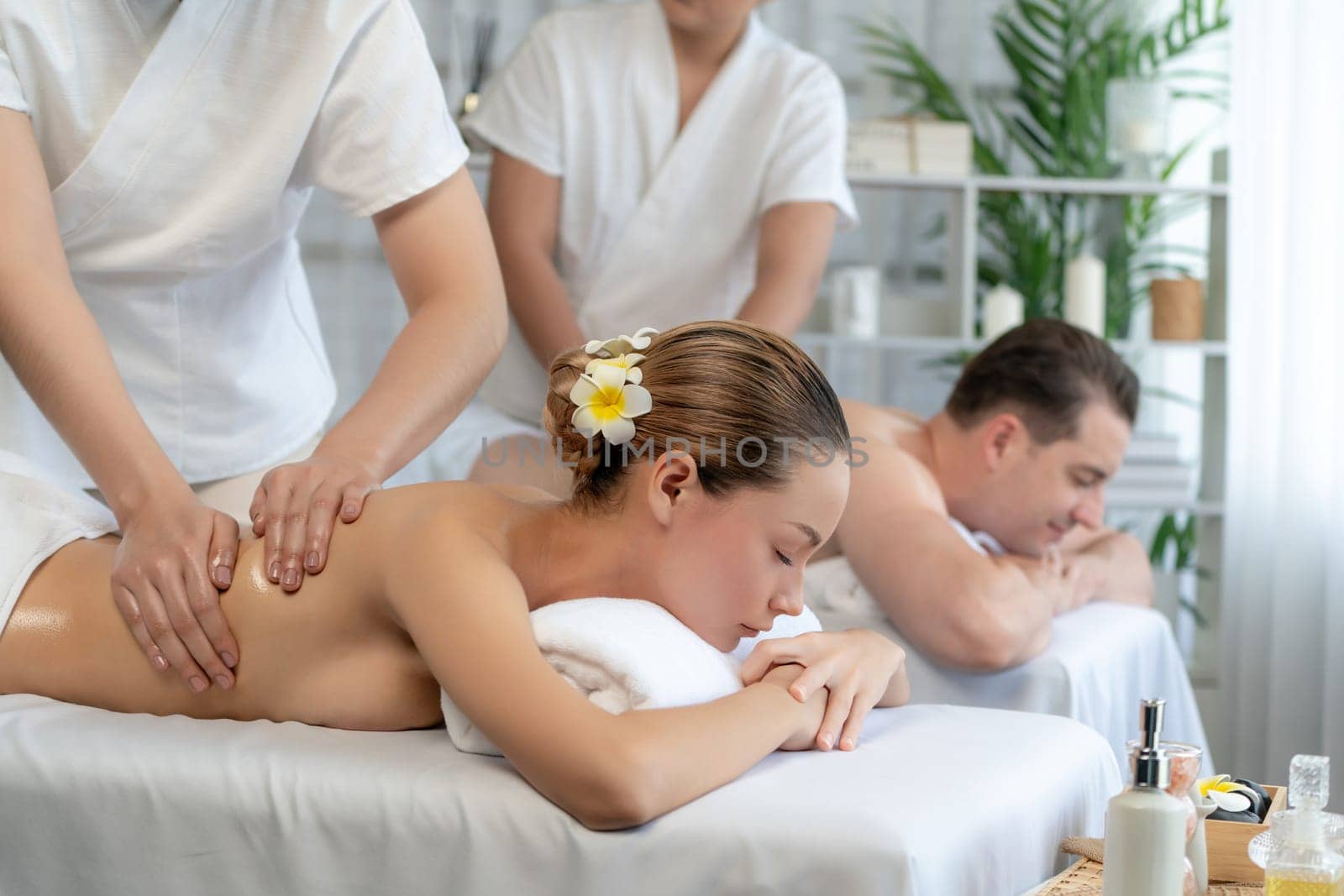 Caucasian couple customer enjoying relaxing anti-stress spa massage and pampering with beauty skin recreation leisure in day light ambient salon spa at luxury resort or hotel. Quiescent