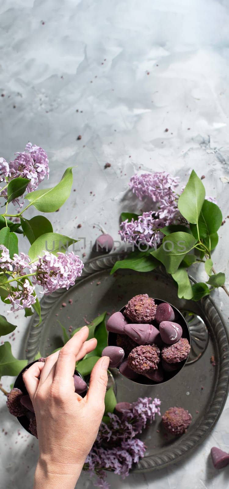 woman's hand takes cuberdon praline from a candy bowl, Belgian sweets in glasses, spring still life with a lilac branch by KaterinaDalemans