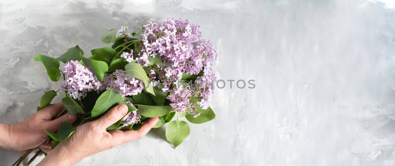 female hands make up a bouquet with a branch of purple lilac on a silver plate on a cement gray background with space for text concept of early spring flowers, High quality photo